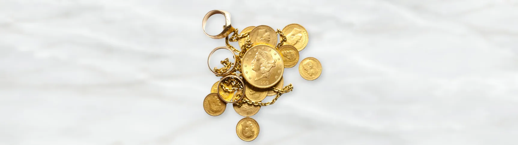 Zwölf goldene Münzen in verschiedenen Größen, mit einer Goldkette und drei goldenen Ringen. Der Hintergrund ist hell gehalten.